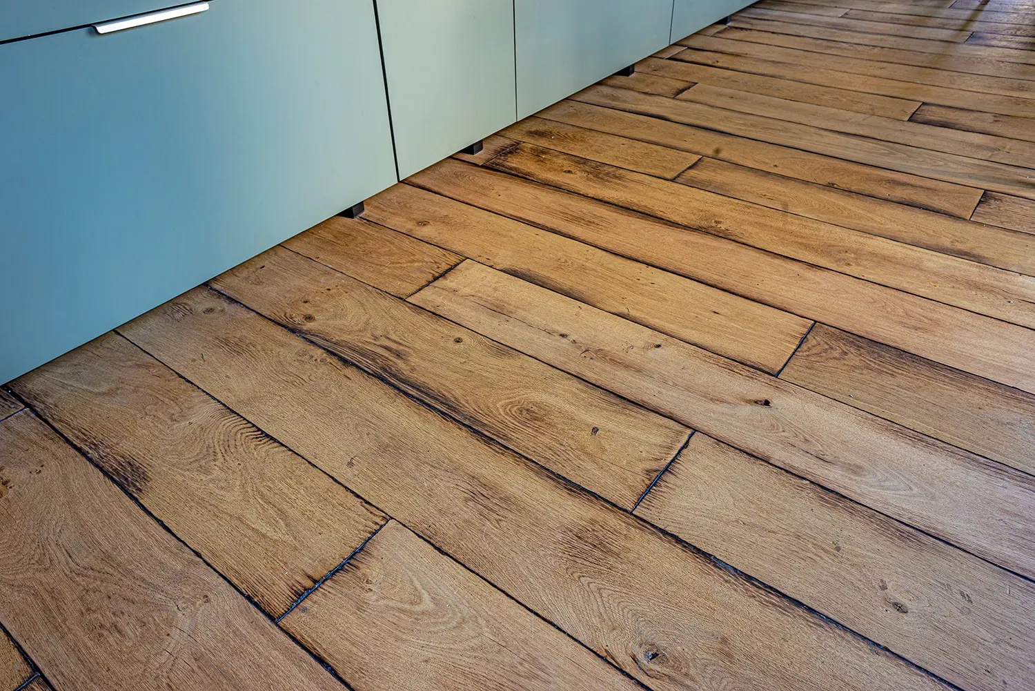 Détail du parquet chêne brossé en lames larges devant les meubles bas de la cuisine